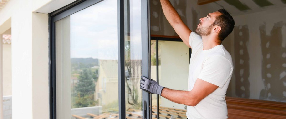 handsome young man installing bay window in a new house construction site
